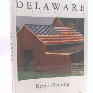 May include: A book titled "DELAWARE DISCOVERED" by Kevin Fleming. The cover features a barn with a roof painted as the American flag. The barn is red with a blue and white roof. The book is a Portfolio Press publication.