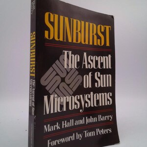 May include: A hardcover book titled "SUNBURST The Ascent of Sun Microsystems" by Mark Hall and John Barry. The cover is black with yellow and white text. The book's spine also displays the title.