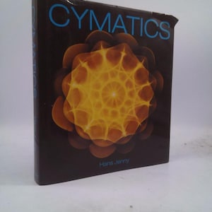 May include: A book titled "Cymatics" by Hans Jenny. The cover features a dark brown background with a bright yellow and orange geometric pattern in the center.