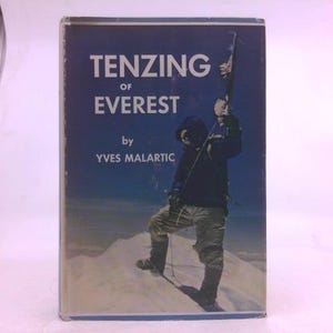 May include: A vintage book titled "Tenzing of Everest" by Yves Malartic. The cover features a photograph of a person on a snowy mountain, holding a flag. The book has a blue background with white text.