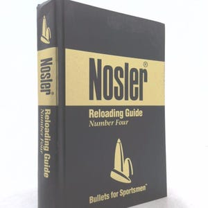 May include: A black hardcover book titled Nosler Reloading Guide Number Four. The cover features a gold horizontal band with the brand name in black, and a gold graphic of two bullets below the text. The spine also displays the title in gold.