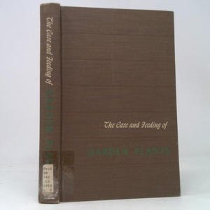 May include: A hardcover book titled "The Care and Feeding of Garden Plants" in a brown cover. The title is printed in a serif font. The spine of the book is visible, with the title printed vertically. The book is on a white background.
