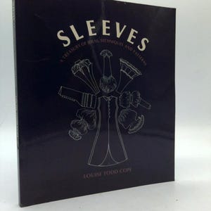 May include: A book titled "Sleeves: A Treasury of Ideas, Techniques and Patterns" by Louise Todd Cope. The cover is dark blue with white text and a line drawing of various sleeve designs. The book is a guide for sewing enthusiasts.