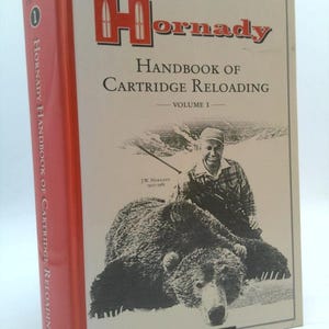 May include: The cover of the sixth edition of the Hornady Handbook of Cartridge Reloading, Volume I. The cover features a black and white illustration of a hunter with a rifle and a bear.