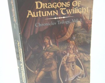 May include: A vintage paperback book titled "Dragons of Autumn Twilight" from the Dragonlance series. The cover features illustrations of two figures and a dragon, with text reading "The New York Times Best-Selling Series".
