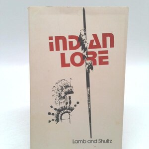 May include: A book cover with the title "INDIAN LORE" in red letters. The cover also features a black and white illustration of a Native American headdress and a spear. The author's names, "Lamb and Shultz", are printed in black at the bottom of the cover.