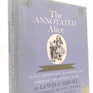 May include: A hardcover book titled "The Annotated Alice" by Lewis Carroll. The cover is a light purple with white text and an illustration of Alice. The book's title is in large, bold letters.