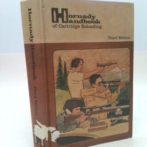 May include: A vintage "Hornady Handbook of Cartridge Reloading" book, Third Edition. The cover features an illustration of people shooting rifles and handguns. The book's spine and cover are brown and beige.