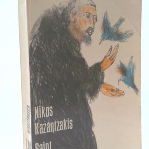 May include: A book cover featuring a black and white illustration of a man with a beard, wearing a dark robe, with two blue birds flying around him. The title of the book is "Nikos Kazantzakis Saint Francis" and the author is "Nikos Kazantzakis".
