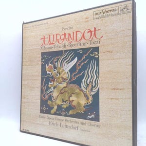 May include: Vintage RCA Victor record album of Puccini's Turandot opera. The album cover features a beige background with the title in large red Japanese characters and a gold dragon illustration. The album includes the names of the performers.