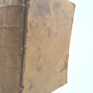 May include: A close-up of the spine of a worn, brown leather-bound book. The book is very old and has a lot of wear and tear.