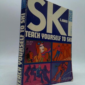 May include: A vintage book titled "Teach Yourself to Ski" with a blue cover and white text. The cover features illustrations of skiers in various poses and a woman with orange hair and goggles. The book is part of the Aspen Ski Masters series.
