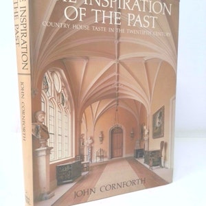 May include: A book titled "The Inspiration of the Past: Country House Taste in the Twentieth Century" by John Cornforth. The cover features a photograph of a grand, vaulted hallway with a wooden floor and a large window.