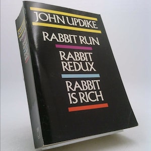 May include: A hardcover book titled "Rabbit Run" by John Updike. The book has a black cover with the title in white, and the author's name in yellow. The book's spine is visible, and the book is slightly angled.