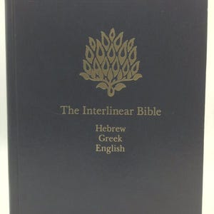 May include: A black hardcover book titled The Interlinear Bible with Hebrew, Greek, and English text printed in gold on the front cover. Above the title is a gold graphic illustration of a stylized tree with leaf-shaped elements.