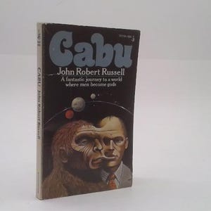 May include: A vintage paperback book titled "Cabu" by John Robert Russell. The cover features a dark background with the title in light blue and an illustration of a man morphing into an ape-like figure. The tagline reads "A fantastic journey to a world where men become gods."