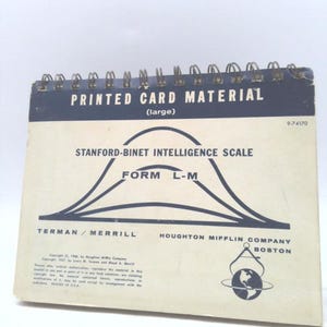 May include: A spiral-bound book titled "PRINTED CARD MATERIAL" with the text "STANFORD-BINET INTELLIGENCE SCALE" and "FORM L-M". The cover is cream-colored with black text and graphics. The book is a vintage educational tool.