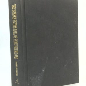 May include: A hardcover book titled "The Science Fiction Hall of Fame Volume One" by Robert Silverberg. The book has a black cover with gold lettering on the spine. The book is in good condition.