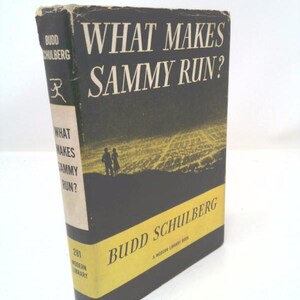May include: A black and yellow paperback book titled "What Makes Sammy Run?" by Budd Schulberg. The book cover features a cityscape with two figures standing in the foreground.