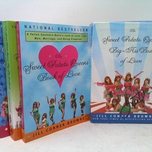 May include: A stack of books, including "The Sweet Potato Queens' Book of Love" and "The Sweet Potato Queens' Big-Ass Box of Love." The covers feature illustrations of women, hearts, and text. The books are in various colors.