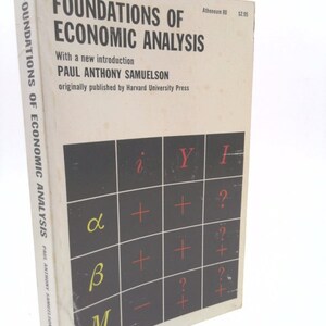May include: A white book with the title "Foundations of Economic Analysis" by Paul Anthony Samuelson. The book cover features a black and white table with red plus and minus signs.