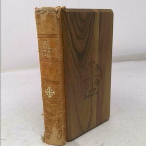 May include: A vintage book titled "The Small House at Allington" by Anthony Trollope. The book is bound in brown leather with gold lettering and a cross design. The book is resting on a wooden bookend with the word "Jerusalem" inscribed on it.