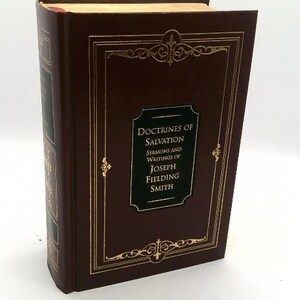 May include: A maroon hardcover book titled Doctrines of Salvation: Sermons and Writings of Joseph Fielding Smith. The cover features gold foil filigree borders and a central black rectangular label with gold lettering. The spine is also gold-embossed.