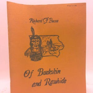 May include: An orange-colored book titled "Of Buckskin and Rawhide" by Richard F. Busse. The cover features a black illustration of a Native American chief and a map. The price is $3.00.