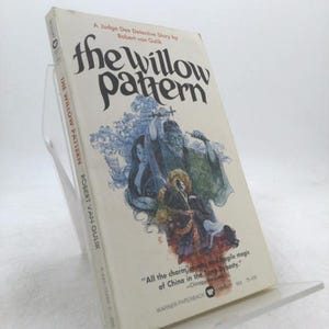 May include: A paperback book titled "The Willow Pattern" by Robert van Gulik. The cover features a blue and white illustration of figures and a pagoda. The book is displayed on a clear acrylic stand.
