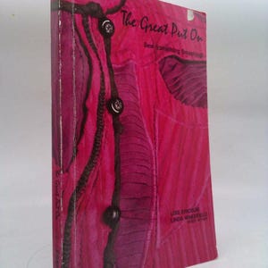 May include: A vintage book titled "The Great Put On" with a vibrant pink cover. The cover features a close-up of a pink garment with black button details and the text "Sew Something Smashing!"