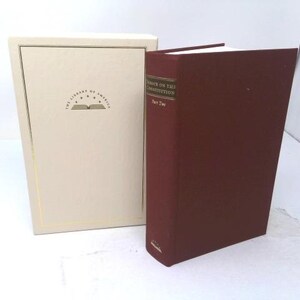 May include: A maroon hardcover book titled Debates on the Constitution Part Two, standing next to a cream-colored slipcase. The slipcase features a gold-bordered rectangular frame and the text The Library of America with a book icon and five stars.