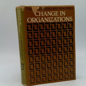 May include: A hardcover book titled "CHANGE IN ORGANIZATIONS" by Paul Goodman and Associates. The book has a brown cover with a repeating black geometric pattern. The spine displays the author's name and the title.