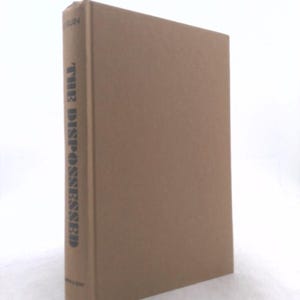 May include: A hardcover book titled The Dispossessed by Le Guin with a plain tan cover. The spine features the title in dark lettering, with the author's name at the top and the publisher's name at the bottom, presented against a neutral background.