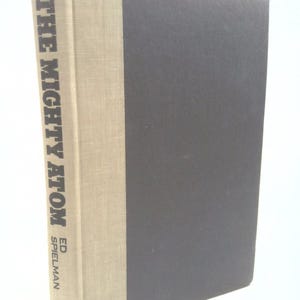May include: A hardcover book titled "THE MIGHTY ATOM" by Ed Spielman. The spine is light beige with the title and author's name in dark text. The cover is dark gray.