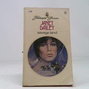 May include: A vintage paperback book titled "Savage Land" by Janet Dailey, published by Harlequin Presents. The cover features a woman's portrait within a circular frame, with a background of a landscape and lightning.