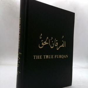 May include: A hardcover book with a black cover. The title "THE TRUE FURQAN" is printed in gold lettering, along with Arabic script. The book's spine also features text. The book is standing upright.