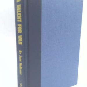 May include: A hardcover book titled A Talent for War by Jack McDevitt. The book features a dark blue spine with gold lettering and a light blue cover. The spine displays the title, author name, and a small publisher logo at the bottom.