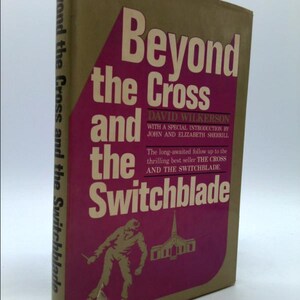 May include: A book cover with a pink background and white text that reads "Beyond the Cross and the Switchblade". The book is by David Wilkerson with a special introduction by John and Elizabeth Sherrill. The cover also features a black and white illustration of a man holding a switchblade in front of a church.