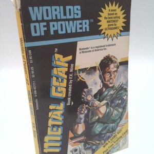May include: A paperback book titled "WORLDS OF POWER" featuring "METAL GEAR" on the cover. The cover art depicts a man in military attire. The book is a novel based on the Nintendo game by ULTRAGAMES.