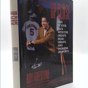 May include: A book titled "Up Close" by Roy Firestone with Scott Ostler. The cover features a photo of Roy Firestone in a brown jacket, smiling, with a baseball jersey with the number 5 and the name "Firestone" on it in the background.