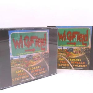 May include: Two CD cases with the title "Wigfield" in red graffiti-style lettering on a green background. The cases feature a road sign design with text and the names Amy Sedaris, Paul Dinello, and Stephen Colbert.