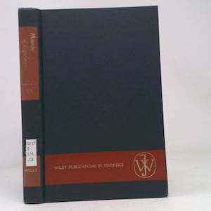 May include: A hardcover book with a black cover and a red band across the bottom. The spine is red with the title "Planning of Experiments" in gold lettering. The book is published by Wiley.