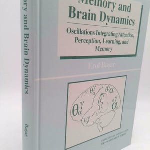May include: A light blue book titled "Memory and Brain Dynamics" by Erol Başar. The cover features text about oscillations, attention, perception, learning, and memory. A diagram of a brain with Greek letters is also visible.
