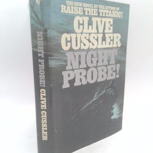 May include: A hardcover book titled Night Probe! by Clive Cussler with a dark blue and black cover featuring a train illustration. The text reads The New Novel By The Author Of Raise The Titanic! Clive Cussler Night Probe! and Bantam.