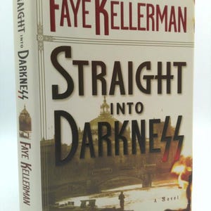 May include: A hardcover book titled "Straight Into Darkness" by Faye Kellerman. The cover features the title in large, dark letters over a sepia-toned image of a city with a bridge and a figure. The author's name is in red.