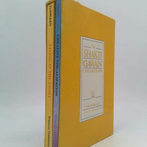 May include: A yellow slipcase containing two books titled The Shakti Gawain Collection. The spines are visible, one yellow with the text Living in the Light and one blue with Creative Visualization. The front cover features a white rectangular label.