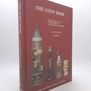May include: A hardcover book titled "THE STEIN BOOK" with a red cover. The cover features illustrations of various beer steins and text including "ILLUSTRATED CATALOG" and "COLLECTOR'S INFORMATION". The book is by Gary Kirsner & Jim Gruhl.