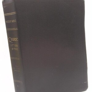 May include: A black hardcover Holy Bible with a textured finish. The spine features gold lettering that reads HOLY BIBLE, Quest STUDY BIBLE, and ZONDERVAN at the bottom. The book is positioned upright, showing the front cover and the spine clearly.