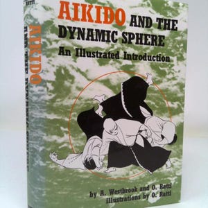 May include: Book cover with a green background and a black and white illustration of two people practicing Aikido. The title of the book is "Aikido and the Dynamic Sphere: An Illustrated Introduction" by A. Westbrook and O. Ratti.