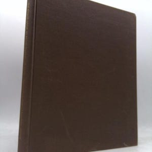 May include: A dark brown hardcover book standing upright. The spine features gold-colored text that reads THE POWER LOOK AT WORK, THE NEW PROFESSIONAL DRESS FOR SUCCESS. The cover has a plain, solid dark brown texture with no other visible markings.